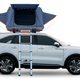 A side profile view of a white Kia SUV with a popped-up Roofnest tent on top.